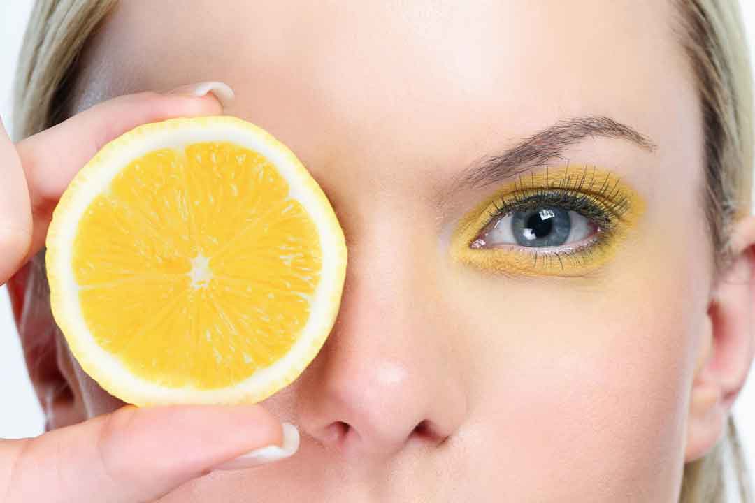 women face with yellow eye shadow and orange slice. First image for article Benefits of vitamin C in skincare– THE ANTI AGING BEAUTY DETECTIVE 